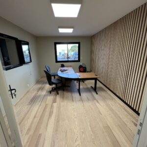Bureau moderne avec parquet clair, mur à lattes de bois, grand bureau incurvé et chaises de bureau. Lumières LED et fenêtre arrière avec vue extérieure.