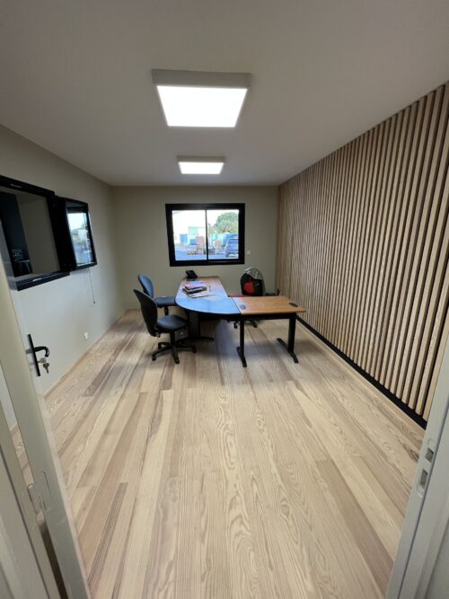 Bureau moderne avec parquet clair, mur à lattes de bois, grand bureau incurvé et chaises de bureau. Lumières LED et fenêtre arrière avec vue extérieure.