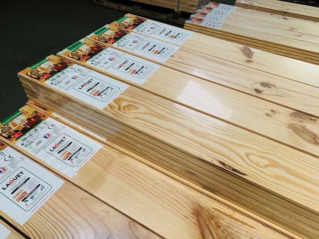 Piles de lames de parquet en bois clair, emballées avec étiquettes LAQUET et dimensions 2000x140x140. Grain naturel visible.