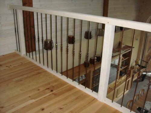 Balustrade bois clair et fer forgé sombre vue d'une mezzanine sur salon-cuisine, sol en pin clair.
