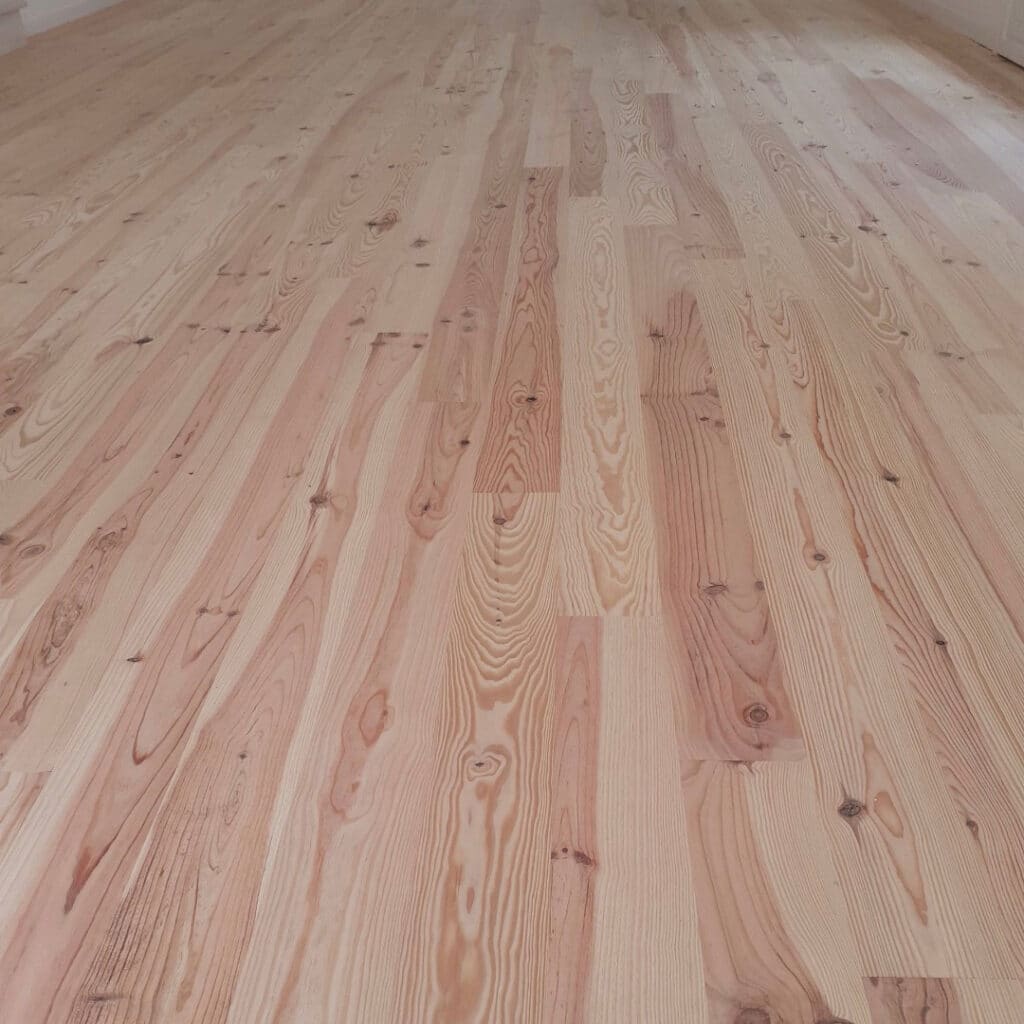 Sol en parquet clair fraîchement posé. Lames de bois naturel avec motifs de grain distincts et nœuds apparents. Ambiance lumineuse et propre.