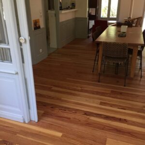 Salle lumineuse avec parquet en bois. Porte française blanche, table et chaises en osier. Grandes fenêtres donnent sur le jardin.