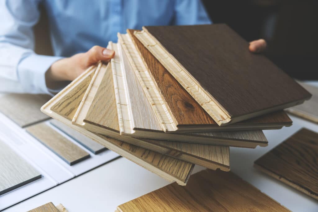 Personne tient des échantillons de parquet en bois clair et foncé, montrant leurs finitions. Des revêtements de sol sont sur la table.