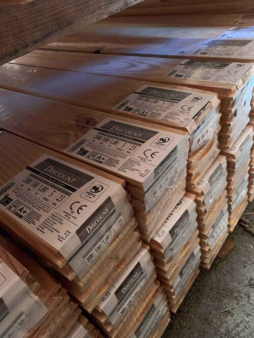 Piles de lames de parquet en pin des Landes "DISCOUNT" emballées. Étiquettes affichent 2000x100x23mm, 1m², 5 lames, PEFC, A+.