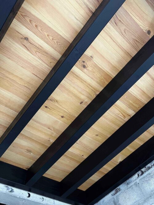 Plafond moderne en bois clair avec poutres sombres diagonales créant un contraste saisissant. Design intérieur contemporain.