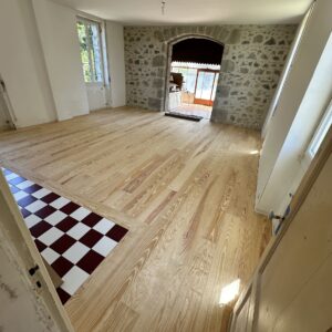 Pièce rénovée avec parquet en pin clair, mur en pierres brutes et carreaux damier. Arche menant à une véranda.