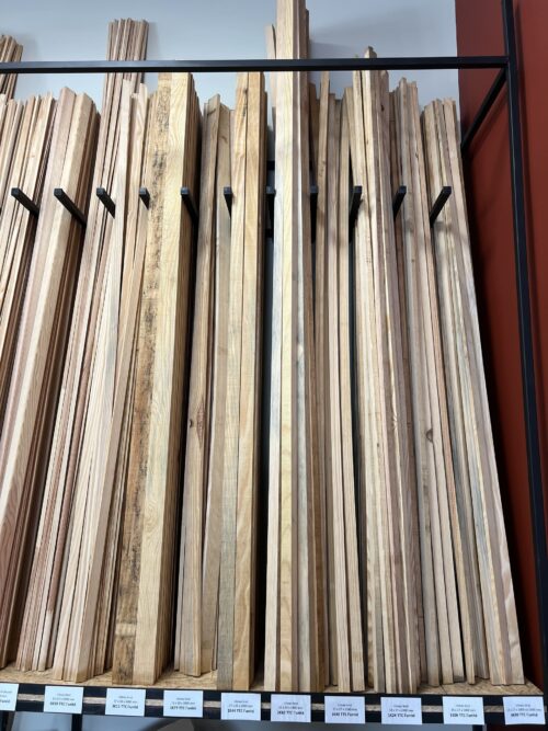 Présentoir de liteaux bruts en bois de diverses dimensions (ex: 8x27mm, 27x50mm) avec étiquettes de prix de 0€68 à 3€11 TTC.